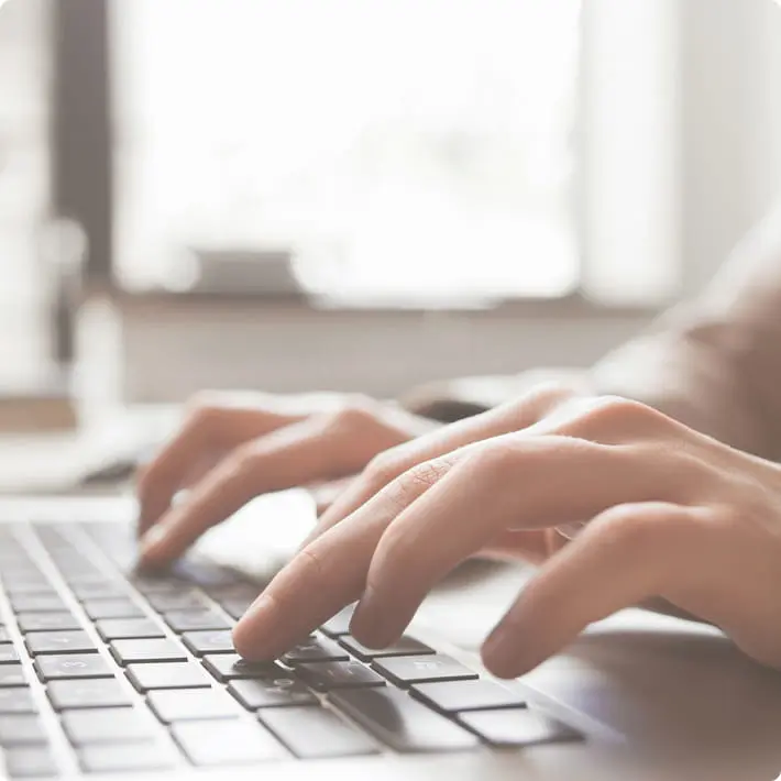 青空の下、黄金色に実った田んぼの中に立つ生産者の男性と、奥に広がる山々の風景