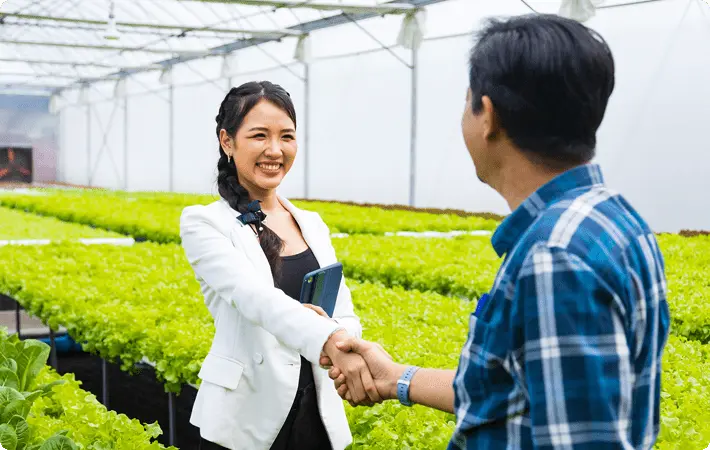 温室栽培の現場で、生産者と支援担当者が握手を交わし協力関係を築く様子
