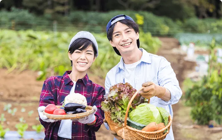 畑で収穫した新鮮な野菜を手に、笑顔で立つ生産者の男女